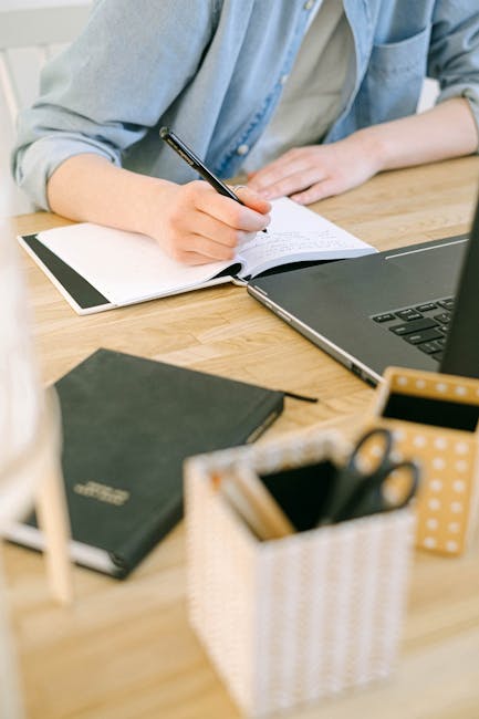 pexels-photo-4240497-4240497-1 Adult writing notes on a notebook while working on a laptop in a cozy home office environment.